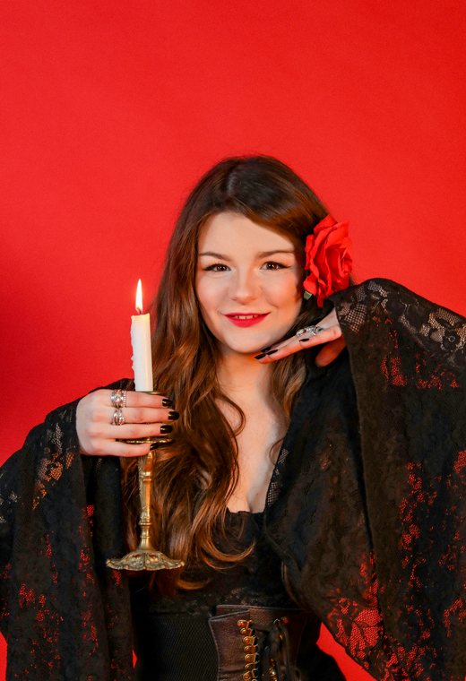 Smiling woman holding a lit candle, a red rose in her hair