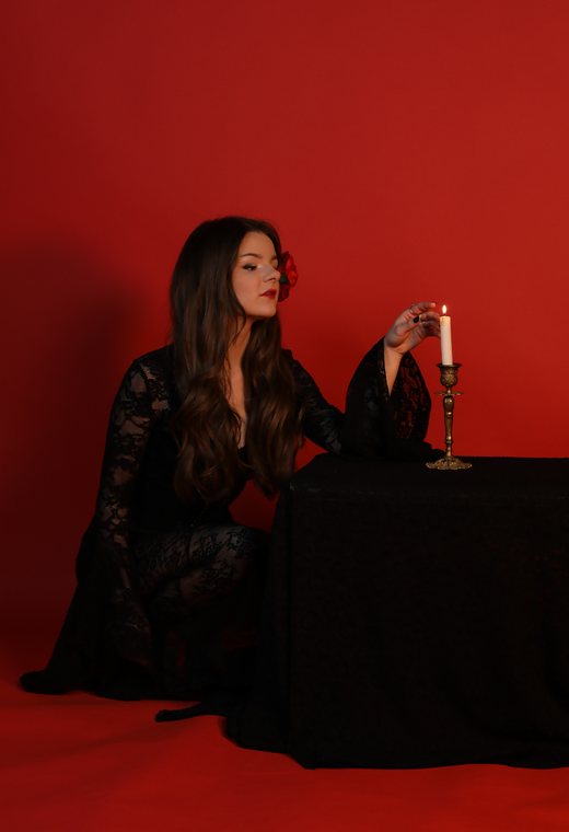 Woman in black lace kneeling at a draped table with a lit candle